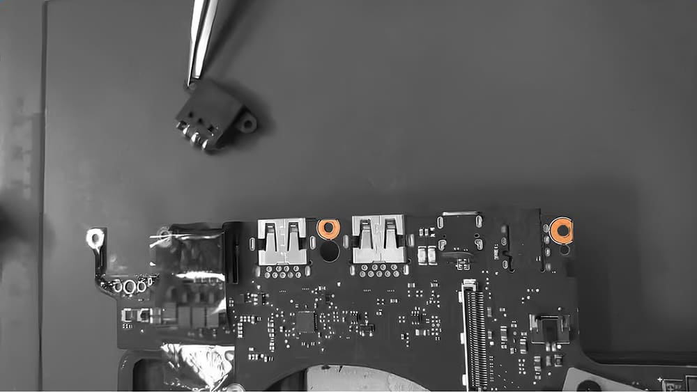 Вид сверху на материнскую плату ноутбука с USB-портами и оранжевыми креплениями, рядом лежит отсоединенный разъем.