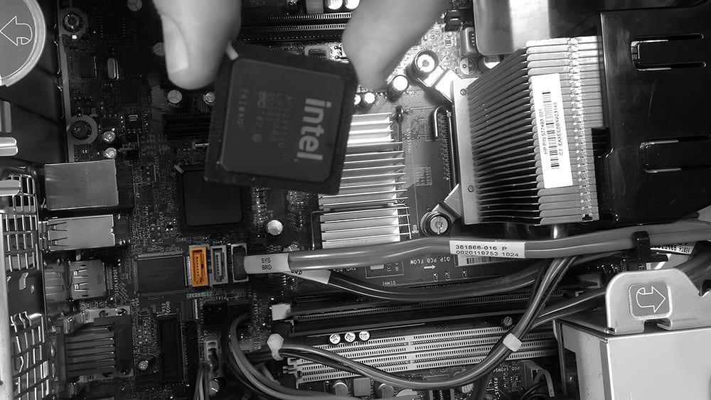 Инженер аккуратно устанавливает процессор Intel в сокет материнской платы, рядом радиатор и провода.
