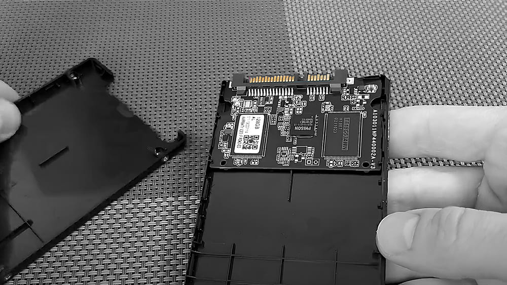 Специалист аккуратно извлекает плату из корпуса SSD-накопителя Phison, готовясь к ремонту или замене компонентов.